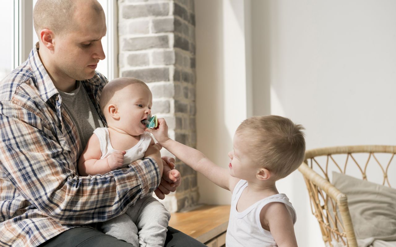 Stående dreng giver baby, der sidder hos far, sut i munden