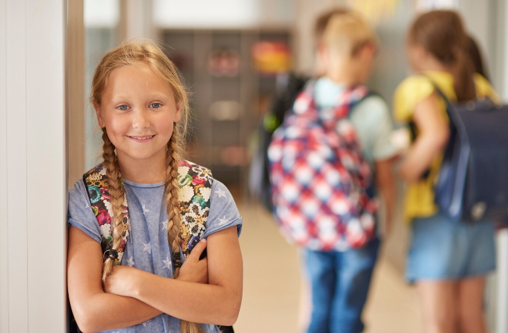 Pige med skoletaske kigger ind i kameraet. I baggrund ses tre kammerater.