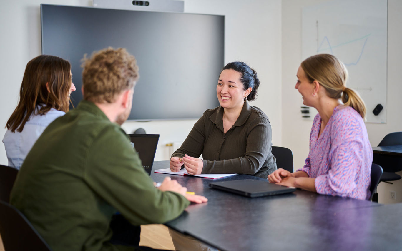 Tre kvinder og en mand sidder rundt om bord og snakker