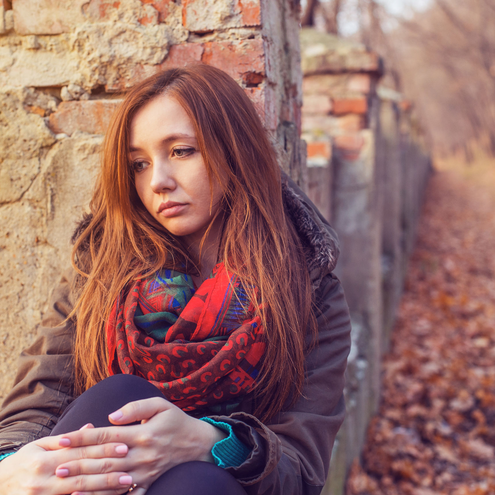 Ung kvinde, der sidder op ad en mur udenfor, og ser meget trist ud