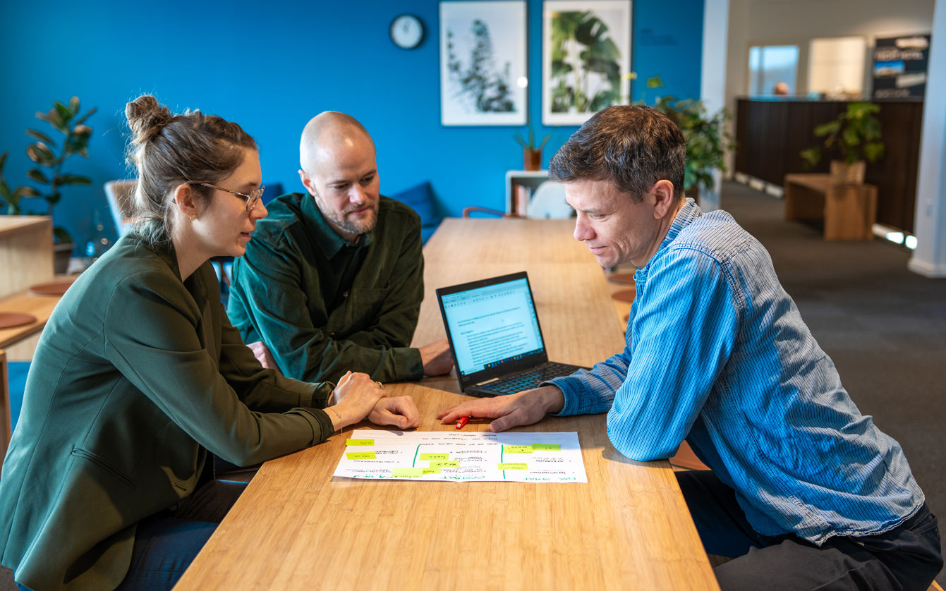 Tre personer der sidder ved et bord med en computer