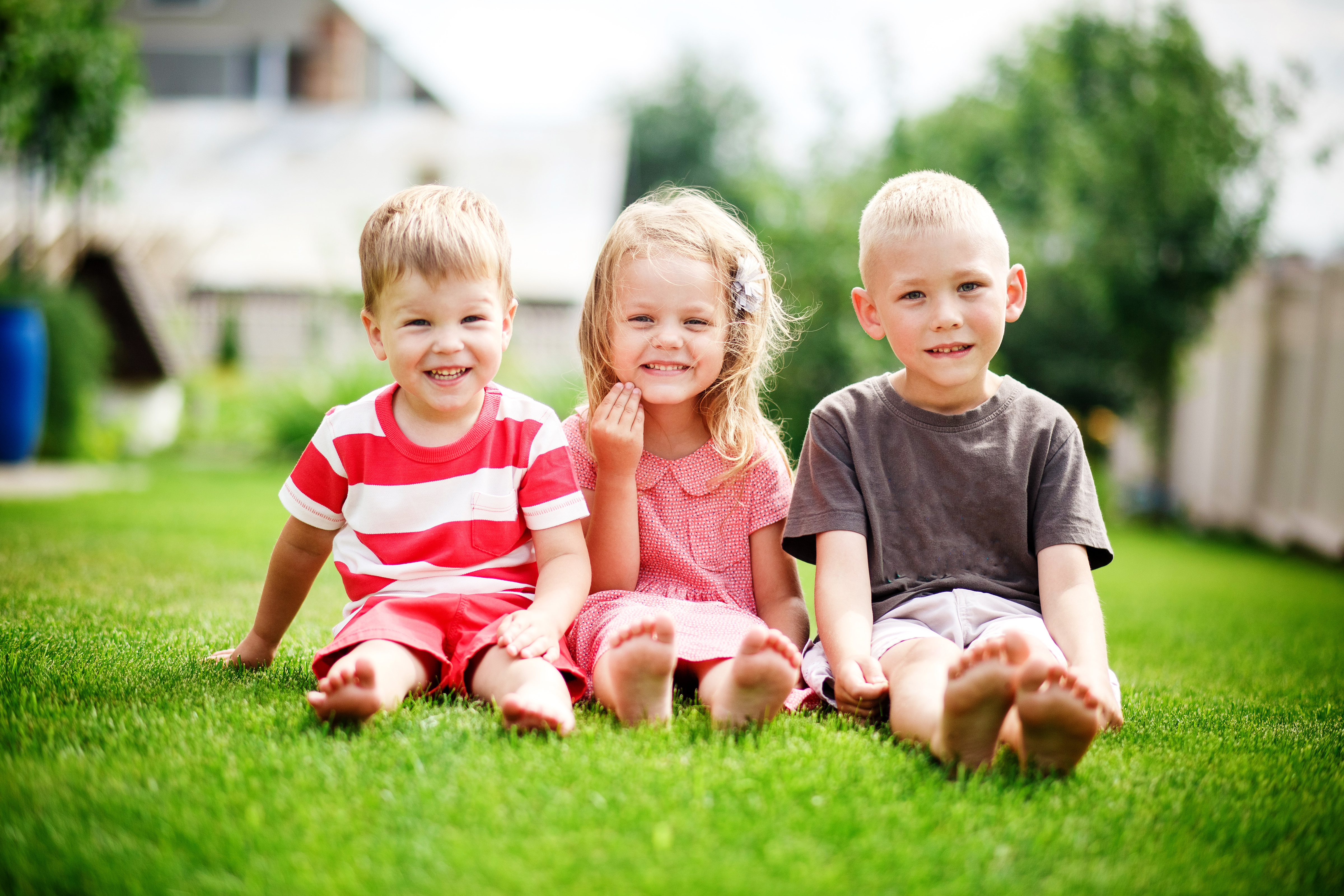 Tre mindre børn sidder på græsset ved siden af hinanden