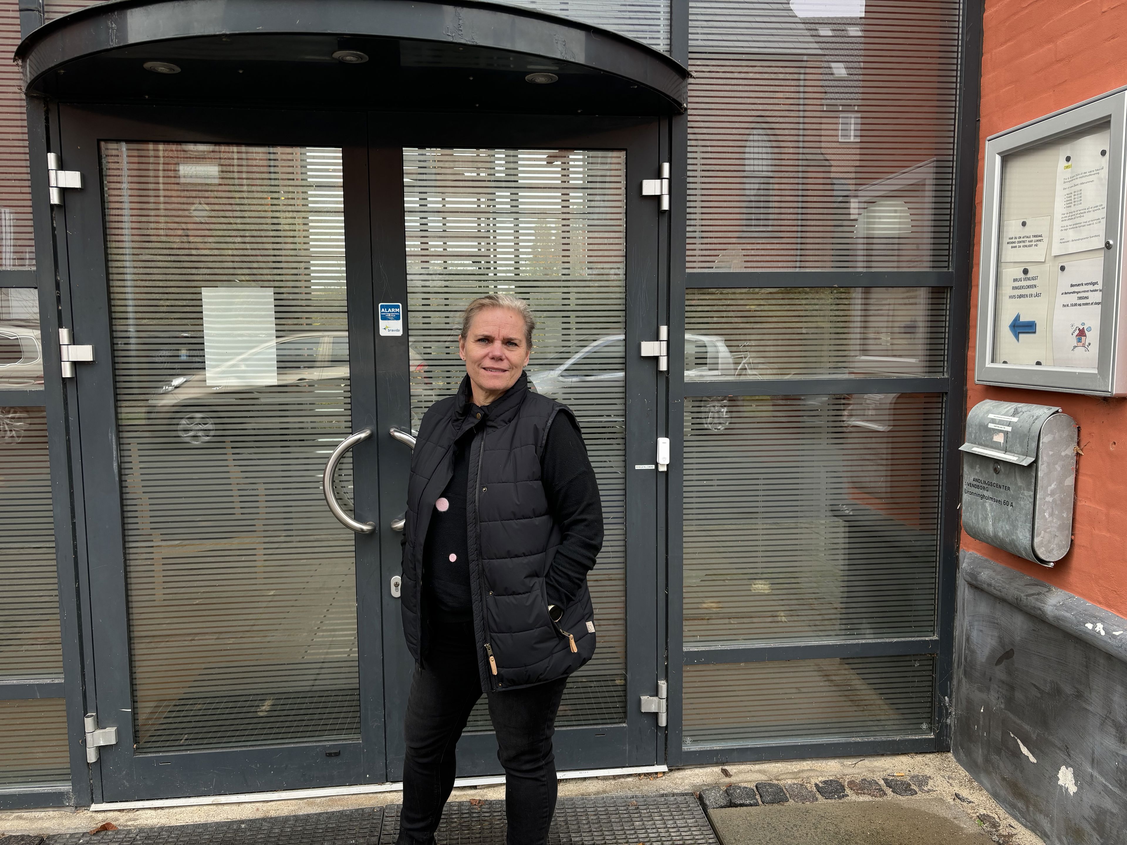 Kvinde i mørt tøj står foran en indgangsdør
