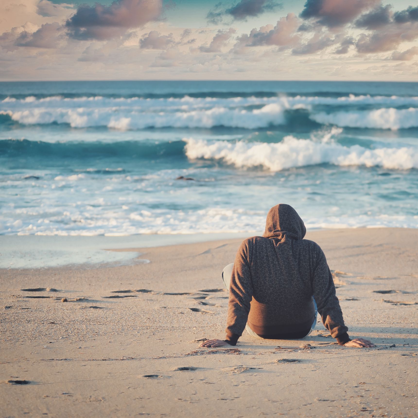 Person, der sidder med ryggen til og kigger på havets bølger