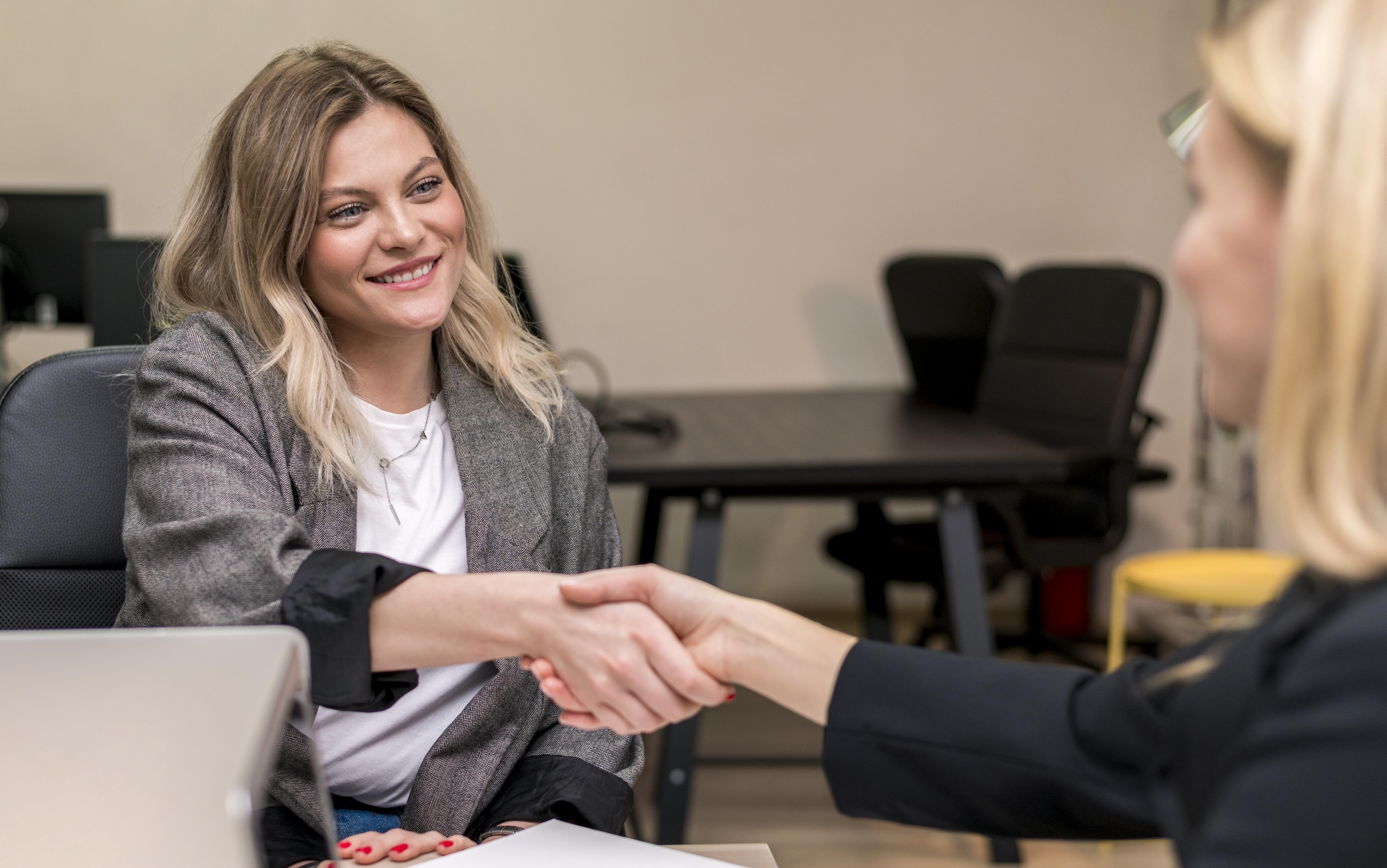To kvinder trykker hånd. Den ene kvinde har en computer foran sig.
