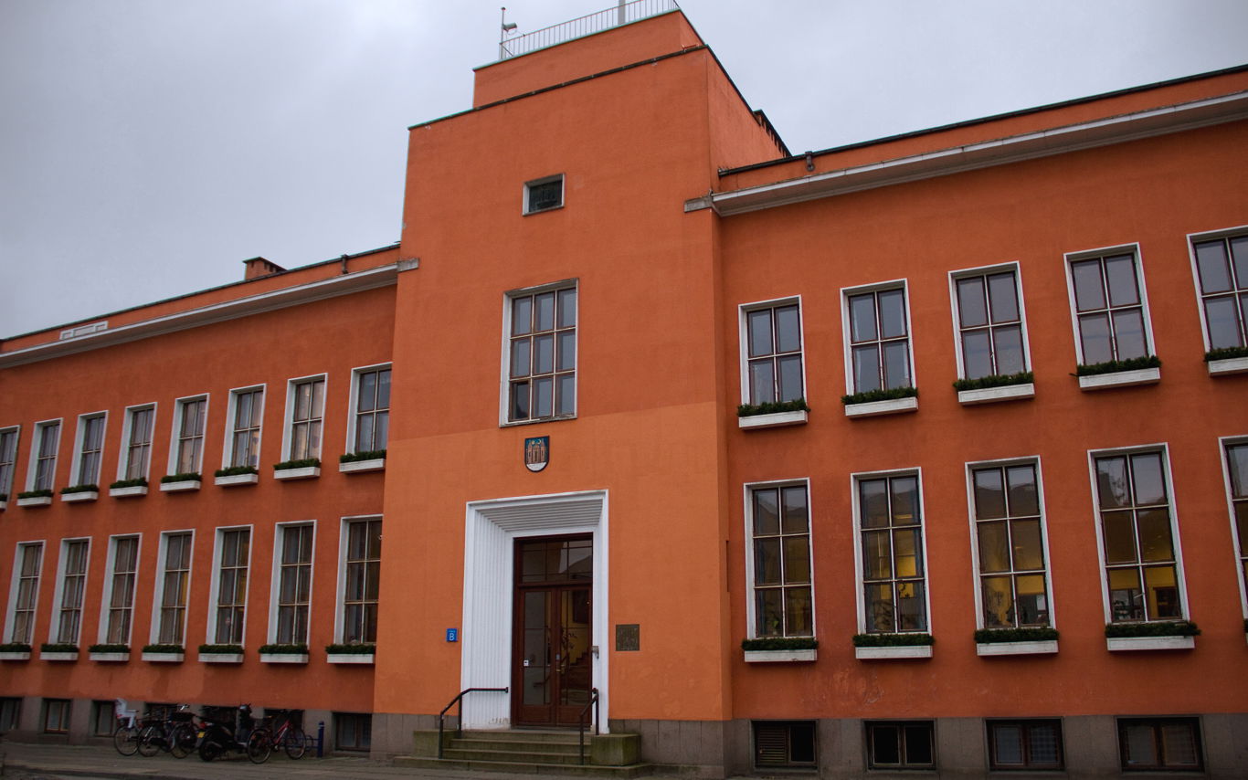 En stor rødlig bygning med brune og hvide vinduesrammer, der viser at bygningen har to etager.