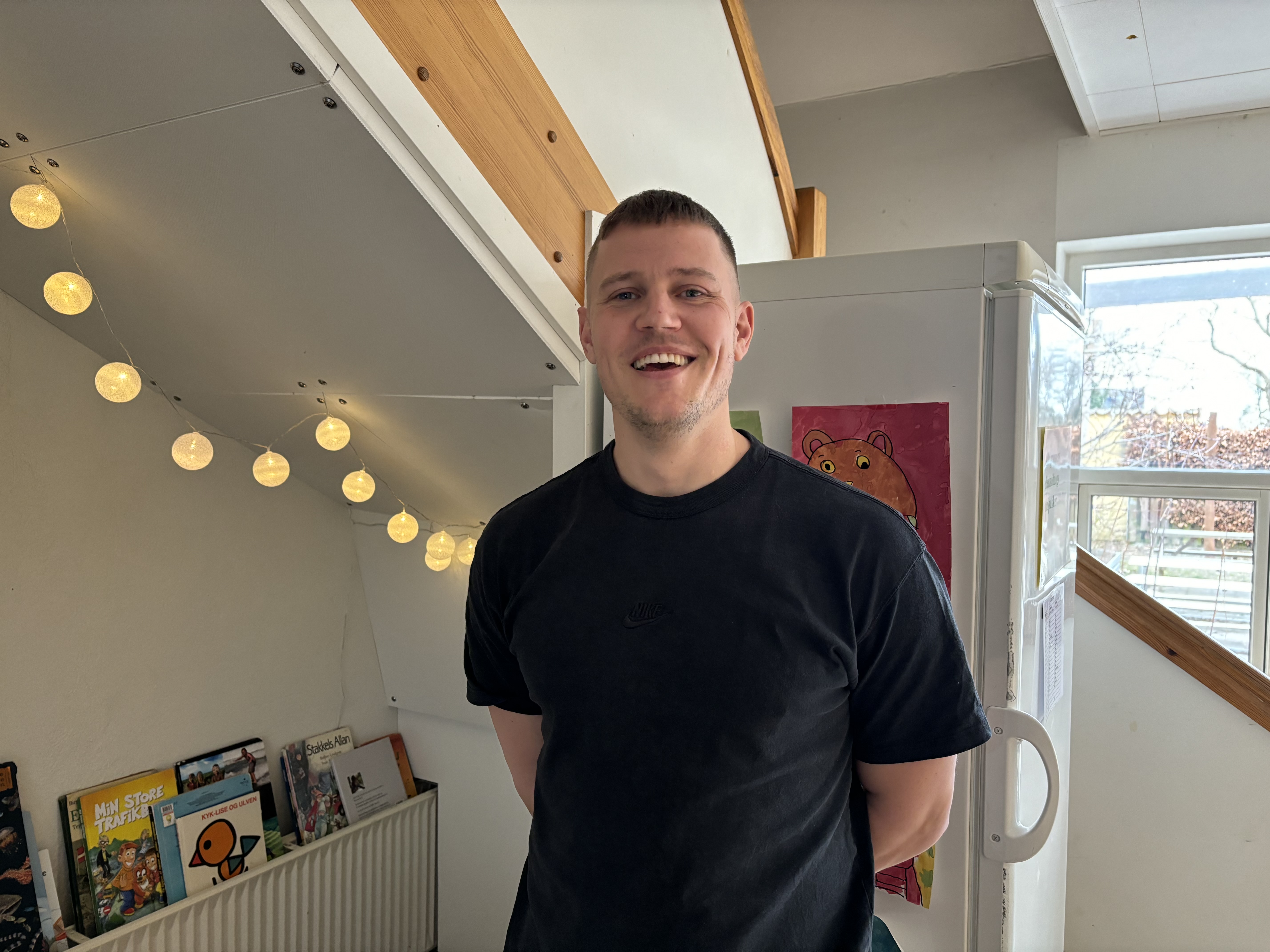 Ung smilende mand stående foran køleskab og bøger