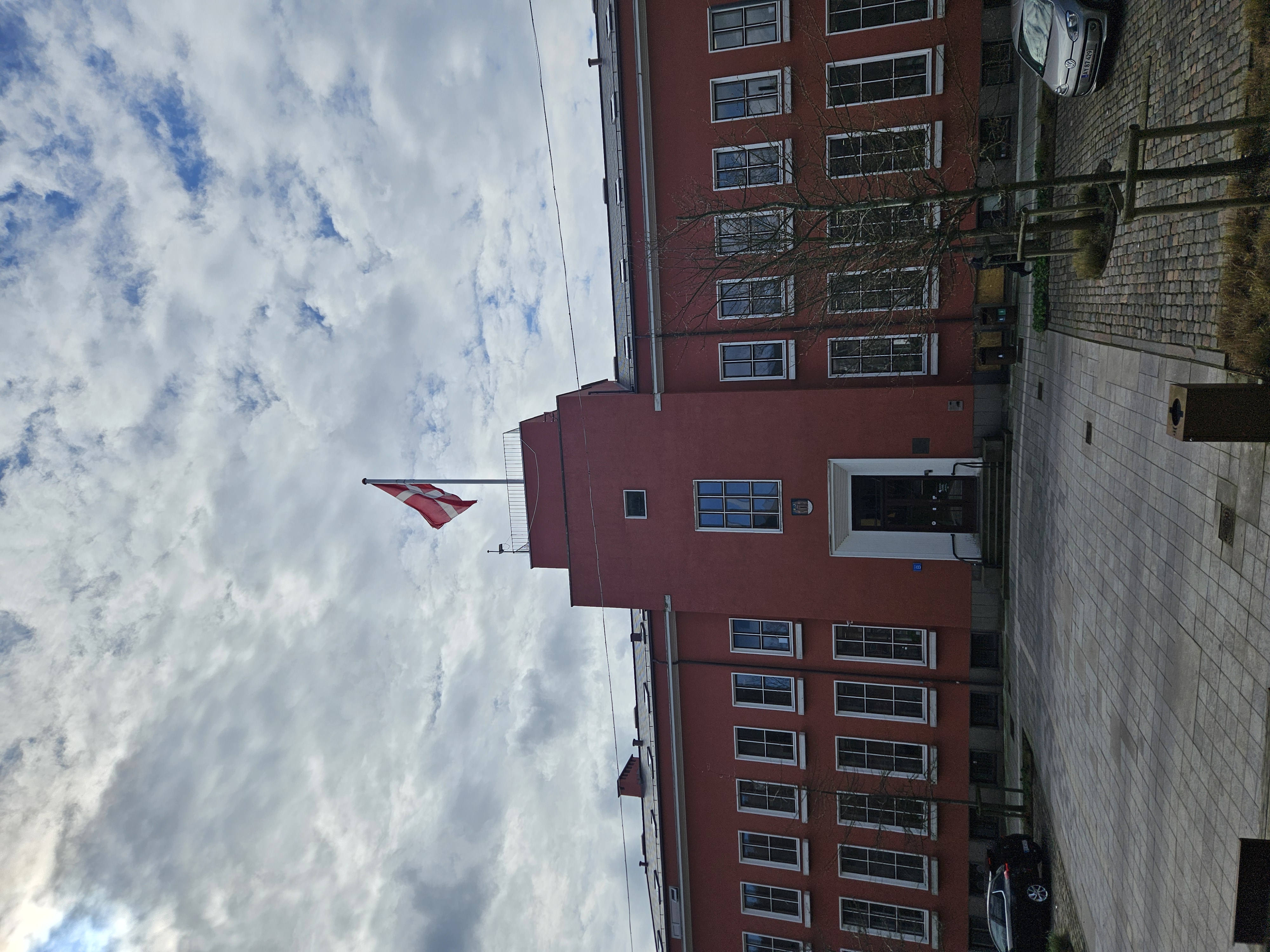 En to-etagers rødlig bygning med hvide vinduesrammer. Øverst på bygningen vejrer Dannebrog. Det er Svendborg Rådhus.